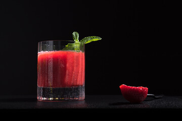 Un vaso de refrescante jugo de fresa triturado decorado con una rama de menta y fresas cortadas sobre un fondo negro