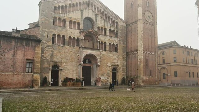 Parma, Emilia-Romagna, Italy. January 2022. Amazing pov footage walking towards the fog-shrouded Duomo square. The cathedral and the baptistery dominate the scene, people cross the square.
