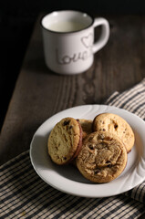 Biscotti al cioccolato e una tazza di latte su sfondo scuro.