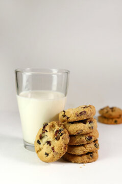 Biscotti al mirtillo con gocce di cioccolato bianco e un bicchiere di latte su sfondo bianco.