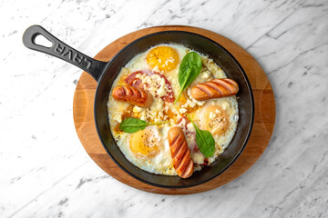 A nutritious breakfast of fried eggs and sausages in a skillet on a marble background. Restaurant banquet menu.