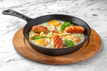 A nutritious breakfast of fried eggs and sausages in a skillet on a marble background. Restaurant banquet menu.