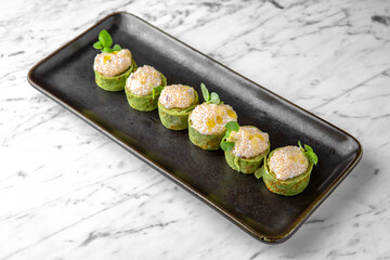 Rolls of spinach pancakes with cheese and pike caviar in a festive plate on a marble background. Restaurant banquet menu.