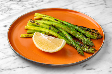 Grilled asparagus with lemon in a festive plate on a marble background. Restaurant banquet menu.