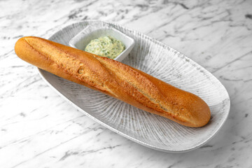 Fresh wheat baguette with butter spread in a festive plate on a marble background. Restaurant banquet menu.