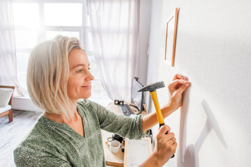Happy smiling middle aged woman hammering nail to wall