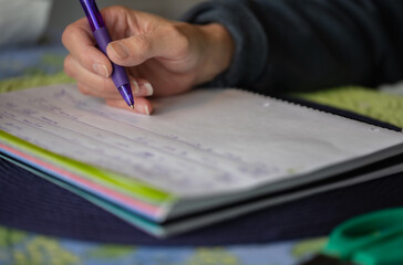 A horizontal photo of a young woman writing in a notebook with a purple pen.