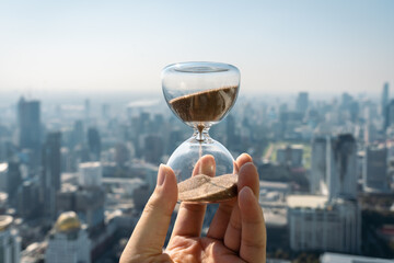Hand holding a Hourglass with cityscape on panoramic skyline and buildings in the morning...