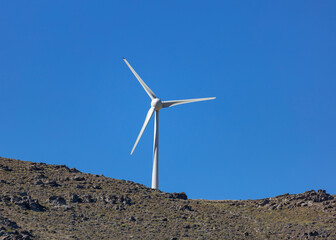 Fototapeta na wymiar Wind turbine on a rocky hill, clear blue sky background, sunny day. Renewable power energy