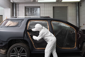 Workwoman in protective suit applying tape on car in service.