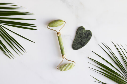 Special devices for Gua Sha - traditional Chinese facial massage. Jade face roller and stone for massage on marble table. Beauty and health care concept. Top view