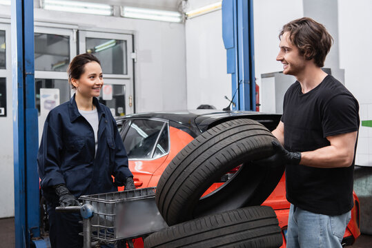 Smiling mechanics standing near tires and blurred car in garage.