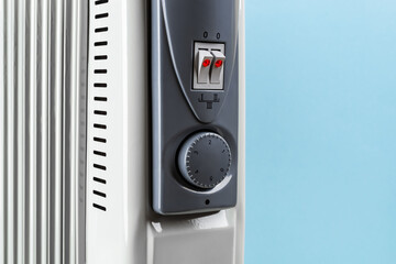Front panel with thermostat knob and two switches of oil filled electric heater against blue background. Portable domestic appliance for heating home in a cold season. Copy space.
