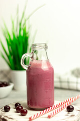 A bottle of cherry smoothies on a white background, cherries in bulk and in a plate. Morning summer breakfast