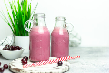 A bottle of cherry smoothies on a white background, cherries in bulk and in a plate. Morning summer breakfast