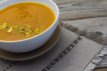 Thick and Creamy Pumpkin Soup in white bowl on wooden rustic background, linen napkin. Healthy eating, horizontal.