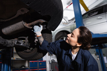 Young mechanic in glove standing near vehicle silencer in service.