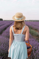 Back view portrait of stylish brunette woman in straw hat walking outdoors on lavender field. Brunette with picnic basket meet the sunset, enjoy the fresh air