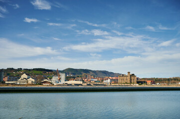 Fototapeta na wymiar View of the Nervion river in the foreground and the industrial zone of Zorroza with a blue sky with clouds