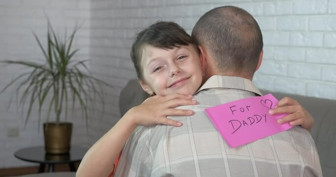 Picture for dad's day. A joyful little girl give a handmade postcard to her father during dad's day at home.
