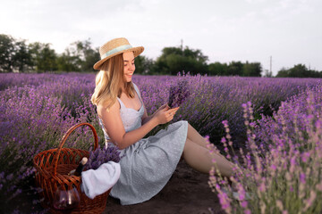 A young beautiful girl sitting among the lavender bushes holding a bouquet of flowers in the summer at sunset. field of blooming lavender and a lady in a hat.