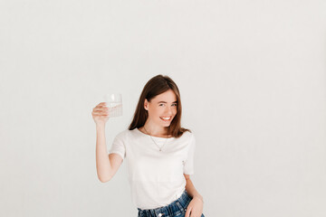 Cheerful pretty woman dressed in casual clothes, holding a glass of pure water high, before having a sip, over white background