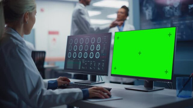 Hospital Research Lab: Female Medical Biotechnology Scientist Working on Green Screen Chroma Key Computer with Brain Scan MRI Images. Background: Neuroscientists Have Meeting Analysing MRI Scan