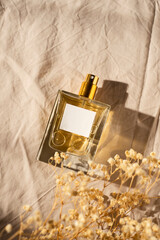 Transparent bottle of perfume on light grey fabric background. Fragrance presentation with daylight...