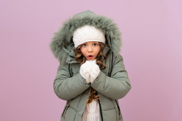 a little girl in winter clothes warms her hands with warm air. the child blows on his hands in the winter season.