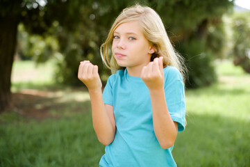 Obraz premium Caucasian little kid girl wearing blue T-shirt standing outdoors doing money gesture with hands, asking for salary payment, millionaire business