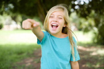 Caucasian little kid girl wearing blue T-shirt standing outdoors pointing displeased and frustrated to the camera, angry and furious ready to fight with you.