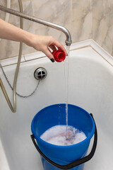 a woman's hand pours detergent from a cap into a bucket of water © Oleg Opryshko