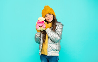 cheerful teen girl in winter clothes hold toy on blue background, valentines day
