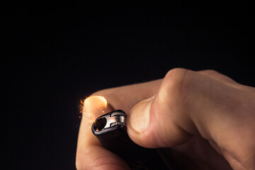 Blazing lighter in hand. Male hand lights the lighter in dark room close up. Flashes of sparks and flame from a lighter on a black background. 
