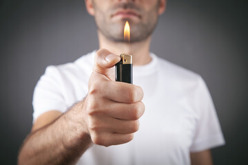 Male hand burning lighter in grey background. - obrazy, fototapety, plakaty