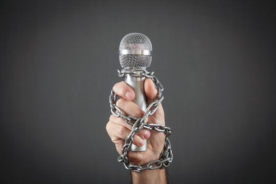 Human hand holding microphone tied with chains.