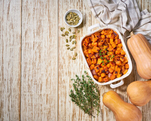 baked butternut squash cubes with thyme and seeds, on a white wooden table, top view.