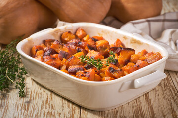 baked butternut squash cubes with thyme on a on a white wooden table.