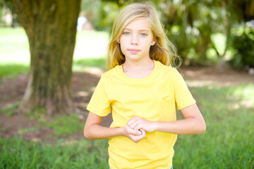 Photo of cheerful confident beautiful Caucasian little kid girl wearing yellow T-shirt standing outdoors arms together