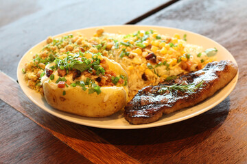 Plate with roasted sirloin steak, farofa, beans, rice with vegetables and baked potato stuffed with cheese and bacon