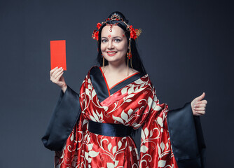 Beautiful young woman in red traditional China costume hold red envelope and showing thumbs up for...