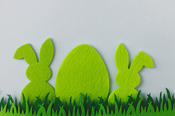 Green Easter egg and bunny in grass on grey background, flat lay with space for text. Happy Easter! Colorful artificial egg and bunny decor. Easter hunt concept