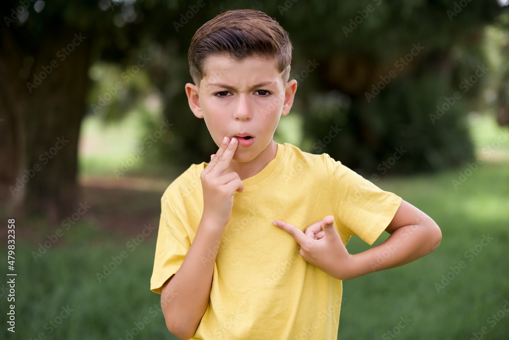 Wall mural Shocked Caucasian little kid boy wearing yellow T-shirt standing outdoor  look surprisedly down, indicates at blank  with fore finger, Scared model - Wall murals