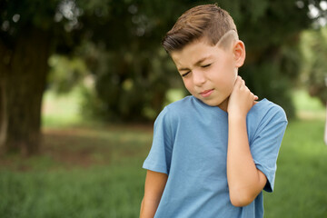 Caucasian little kid boy wearing blue T-shirt standing outdoor Suffering of neck ache injury,...