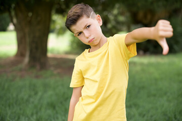 Caucasian little kid boy wearing yellow T-shirt standing outdoor  feeling angry, annoyed,...