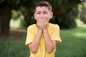 Vivacious Caucasian little kid boy wearing yellow T-shirt standing outdoor , giggles joyfully,...