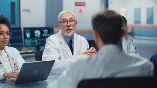 Hospital Conference Meeting Room: Senior Neuroscientist Uses Tablet Computer with MRI Magnetic Resonance Image of the Brain, Talks to Team of Medical Doctors, Neurologists Discuss Patient Treatment