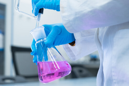 Close up scientist uses a titration method of analysis to study the chemical properties of the water sample. Scientist holding Erlenmeyer flask with pink solution