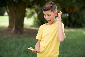 Angry Caucasian little kid boy wearing yellow T-shirt standing outdoors screaming on the phone, having an argument with an employee. Troubles at work.