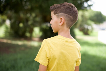 The back side view of a Caucasian little kid boy wearing yellow T-shirt standing outdoors. Studio...